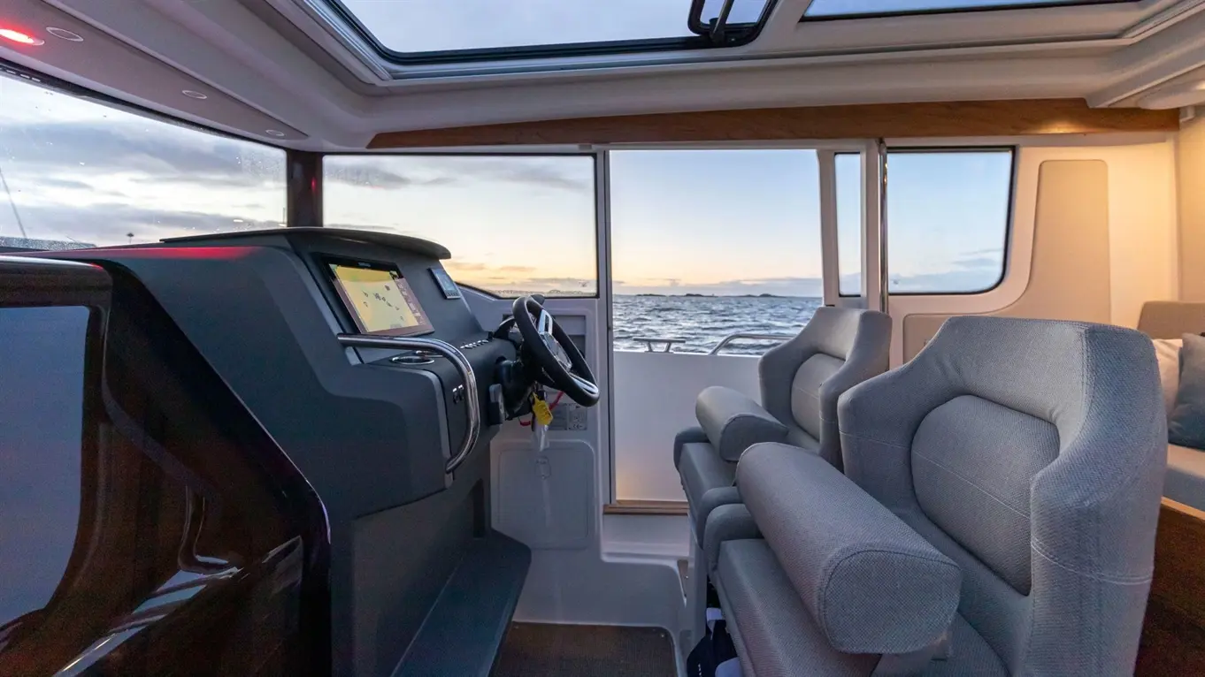 Modern boat interior featuring a steering wheel, navigation screen, and comfortable seating with a view of the sea at sunset.